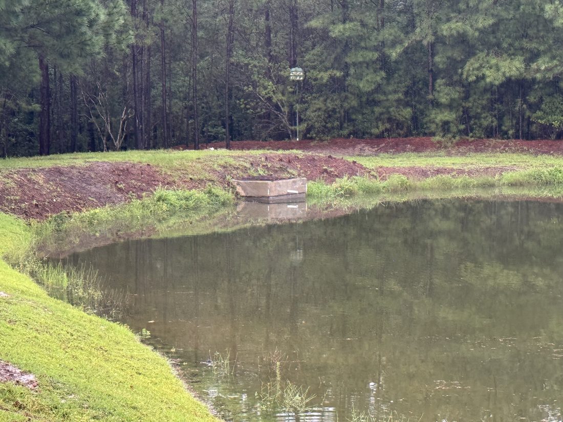 Concrete outlet structure at the edge of a wet pond with a newly graded grassy bank